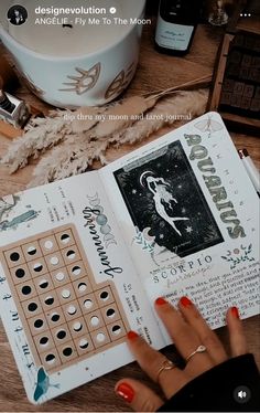 a woman's hand is holding an open book on top of a wooden table