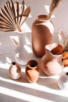 several vases with different shapes and sizes on a white tablecloth in the sun