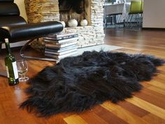 a black sheepskin rug on the floor next to a bottle of wine and glasses