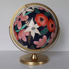 a decorative globe with flowers painted on it's sides and gold base, sitting on a white surface