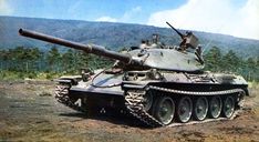 an old tank sitting on top of a dirt field in front of some trees and mountains