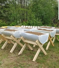 rows of canoes lined up on wooden boards in the grass with trees in the background