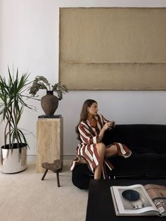 a woman sitting on top of a black couch next to a potted plant in a living room