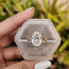 a person holding an engagement ring with a diamond in it's hand, on top of a hexagonal box