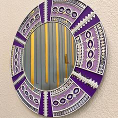 a circular mirror with purple and yellow designs on the front, against a white wall