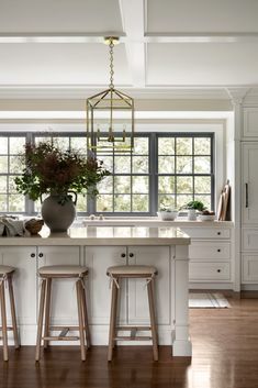 a kitchen island with stools and a potted plant on it in front of a window