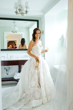 a woman standing in front of a mirror wearing a wedding dress and holding a bouquet