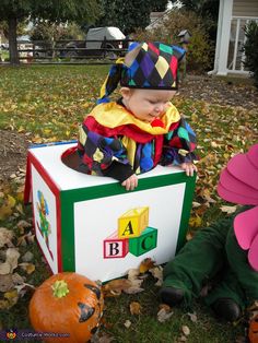 two toddlers dressed as clowns sitting on top of a box in the grass