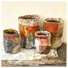 four vases sitting on top of a table covered in different colored paint and paper