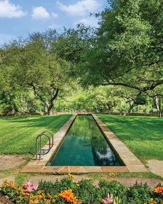 a long pool in the middle of a lush green field with trees and flowers around it