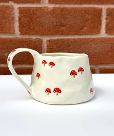 a white coffee cup with red mushrooms on it sitting in front of a brick wall