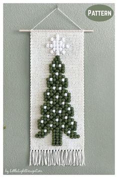 a cross stitch christmas tree hanging on a wall with white and green trimmings