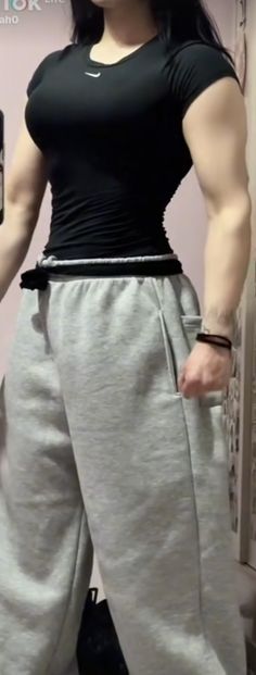 a woman standing in front of a mirror wearing sweatpants and a black shirt with her arms crossed