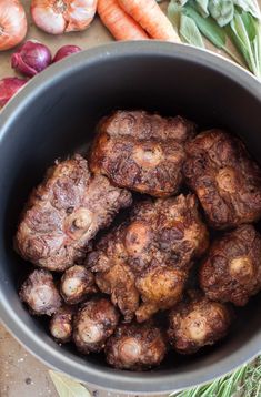 a bowl filled with meat next to carrots and other vegetables on top of a table