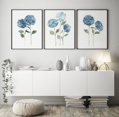 three blue flowers are hanging on the wall above a white dresser and sideboard in a modern living room