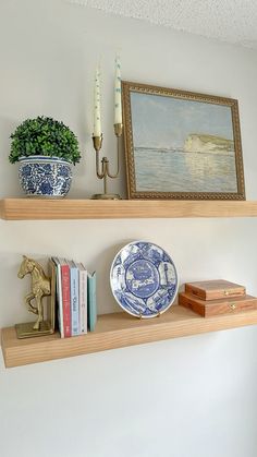 two wooden shelves with books and plates on them, one has a painting above the shelf