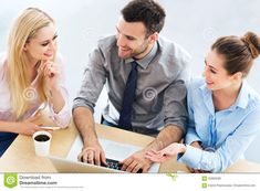 three business people sitting at a table working on a laptop computer and talking to each other