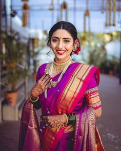 a woman in a purple and gold sari with her hands on her chest, smiling at the camera