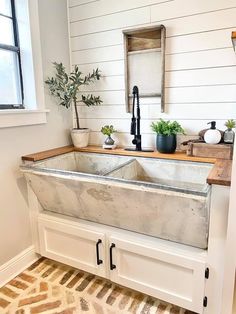 a kitchen sink sitting under a window with potted plants on the counter top in front of it