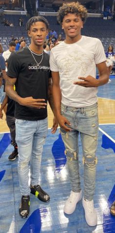 two young men standing next to each other in front of a basketball court with fans