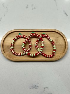 three red and green bracelets sitting on top of a wooden tray next to a marble counter