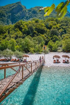 people are sitting on lounge chairs at the end of a pier over clear blue water