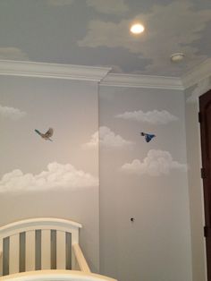 a baby's room with clouds painted on the wall and two birds flying in the sky