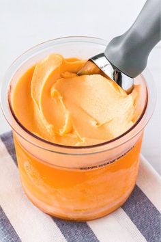 a glass jar filled with orange custard and a plastic spoon in the top