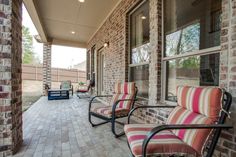 two chairs sitting on the front porch of a brick building with large windows and doors