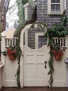 a white gate decorated with greenery and potted plants in front of a house