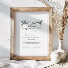 a wooden frame holding a certificate next to a vase with dried flowers and a cross on it