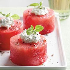 watermelon and goat cheese appetizers on a white plate with a glass of water in the background