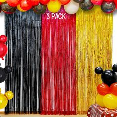 mickey mouse balloons and streamers are on display at a party with the backdrop painted red, yellow, and black