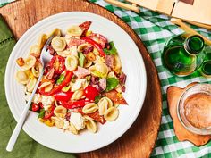 a white plate topped with pasta salad next to a glass of green juice and utensils