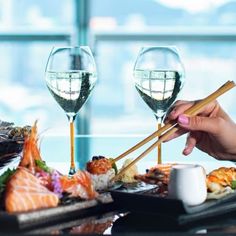 a woman is eating sushi with chopsticks and wine glasses on the table