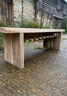 a wooden bench sitting on top of a gravel road next to a building and trees