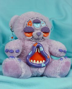 a pink teddy bear with an open mouth and teeth on it's face, sitting against a blue background