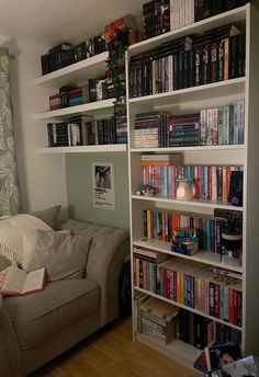 a living room filled with lots of books on top of a white book shelf next to a window