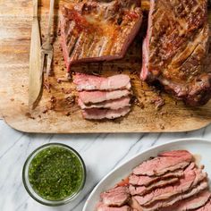 sliced meat on a cutting board next to a bowl of pesto