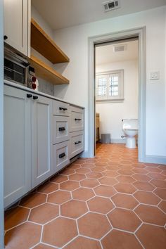 an empty kitchen with white cabinets and brown floor tiles on the floor, along with open shelves