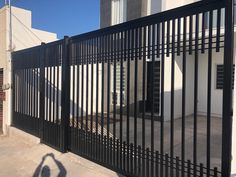 the shadow of a person standing in front of a black gate on a sidewalk next to a building