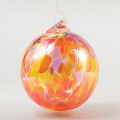 a glass ornament hanging from a string on a white background with an orange and pink design