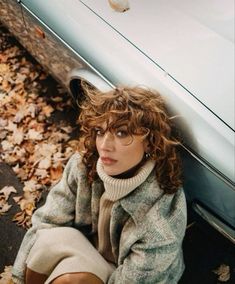 a woman sitting on the ground next to a car with leaves all over her feet