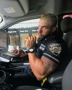 a man sitting in the back seat of a car using a laptop computer while wearing a police uniform