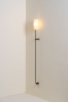 a wall mounted light on the side of a white wall next to a black pole