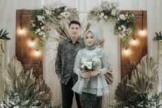 a man and woman standing next to each other in front of a backdrop with flowers