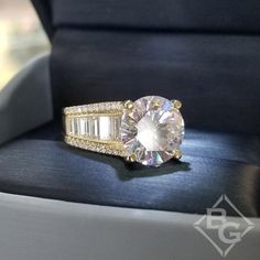 a diamond ring sitting on top of a black cushion in a box with gold trimmings