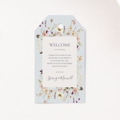 a welcome card with flowers on it and a white tag hanging from the side that says, welcome