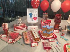 a table topped with lots of cupcakes and desserts next to red balloons