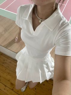 a woman in white shirt and skirt holding a tennis racquet on top of a hard wood floor